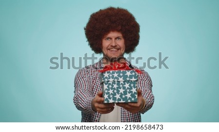 Positive smiling bearded man presenting birthday gift box stretches out hands, offer wrapped present career bonus, celebrating party. Young adult guy boy isolated alone on blue studio wall background
