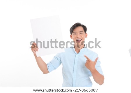 Place For Your Ad. Portrait of smiling asian guy holding empty blank board isolated on white studio background. Happy guy standing with white square paper for template and pointing at it