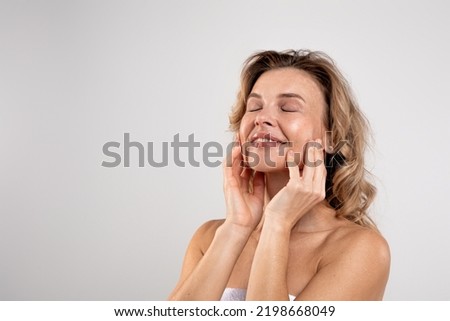 Spa Treatments. Portrait Of Attractive Middle Aged Woman With Beautiful Skin Touching Her Face While Posing Over Light Grey Studio Background, Smiling Lady Wrapped In Bath Towel Enjoying Beauty Care Royalty-Free Stock Photo #2198668049