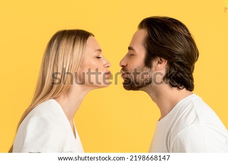 Cheerful millennial caucasian man and blonde lady in white t-shirts are kissing, isolated on yellow background, close up, profile. Couple relationship, love, romantic, ad and offer, facial expression Royalty-Free Stock Photo #2198668147