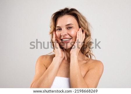 Antiage Skincare. Happy Attractive Middle Aged Female Touching Face And Smiling At Camera, Beautiful Woman With Flawless Skin Standing Wrapped In Towel Over Light Studio Background, Copy Space Royalty-Free Stock Photo #2198668269