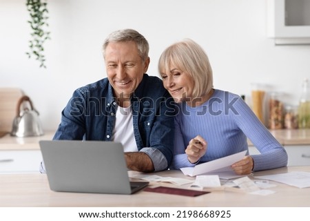 Happy couple of pensioners senior husband and wife sittting in front of computer at kitchen, reading emails, checking bills and correspondence, working on family budget together, copy space Royalty-Free Stock Photo #2198668925