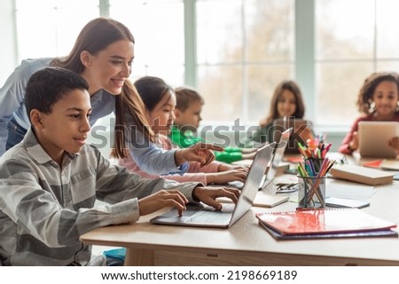 Teacher Teaching Diverse School Kids Using Laptop In Classroom. African American Schoolboy And Diverse Classmates Browsing Internet On Computer Learning Online Indoor. E-Learning Concept Royalty-Free Stock Photo #2198669189