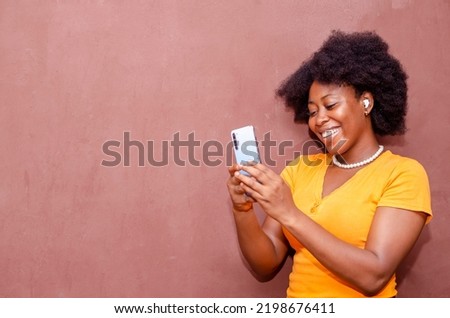 over excited black woman using smartphone listening to music online standing on brown background, copy space Cool gadget and application.Selective focus 