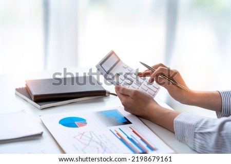 crop shot of business woman checks her work and uses a calculator to calculate her annual financial statements. Turnover and Profit Balance Sheet Making financial records in paper audits. Royalty-Free Stock Photo #2198679161