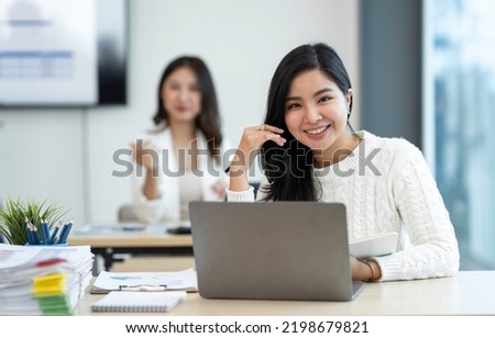 Smiling Asian businesswoman working with a laptop at the office. Looking at the camera.