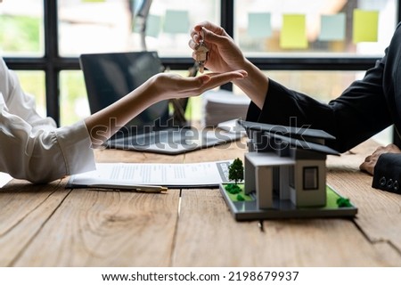 Cropped image of a real estate agent selling broker holds the keys and the model house is given to the customers, home insurance, and Real estate concept.