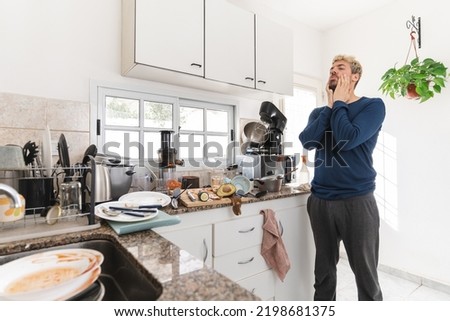 Man looking at the messy kitchen in then morning, full of rubbish and dirty dishes. Morning light apartment Royalty-Free Stock Photo #2198681375