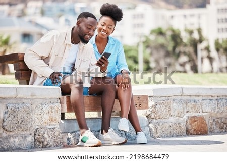 Black couple, love and phone while browsing social media, internet or watching a video while sitting on a park bench. Happy man and woman on a romantic date, trip or summer holiday to relax together