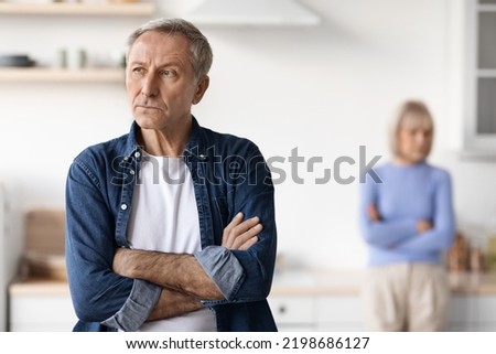 Selective focus on upset mature man with arms crossed on chest looking aside, having quarrel with his wife, kitchen interior. Crisis in marriage for seniors, divorce at older ages concept Royalty-Free Stock Photo #2198686127