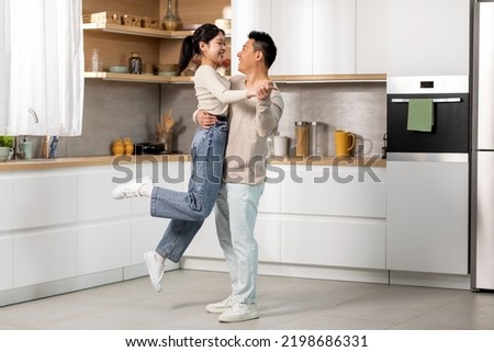 Romantic chinese lovers dancing waltz at kitchen, happy asian young lady enjoying time with her loving middle aged husband at home, cheerful man lifting up his beautiful wife, full length, copy space Royalty-Free Stock Photo #2198686331
