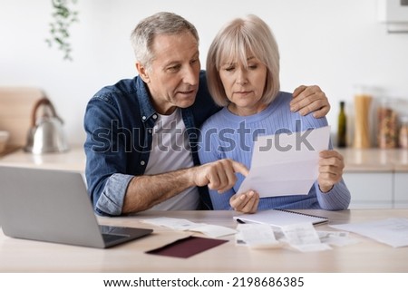 Serious couple of pensioners senior husband and wife sittting in front of computer at kitchen, reading letter, checking bills and correspondence, working on family budget together, copy space Royalty-Free Stock Photo #2198686385
