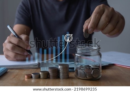 saving money concept. businessman hand holding coins and putting in jug glass using smartphone and calculator to calculate. Money coins stack growing graph and piggy bank. Business, Planning, Target.