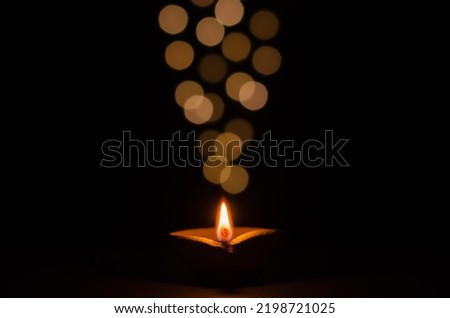 Selective focus on flame of clay diya lamp lit on dark background with bokeh lights. Diwali festival concept.