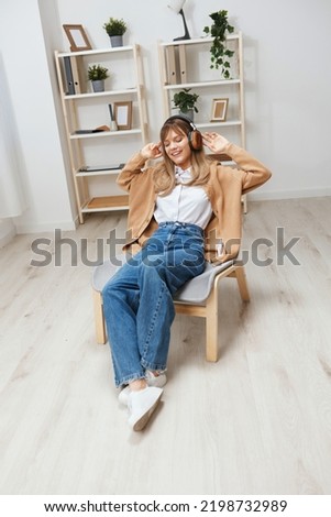 Cheerful young blonde lady in warm sweater in headphones listen enjoy fav songs dancing sitting in armchair at modern home interior. Music time Relaxing Cool playlist Concept. Copy space
