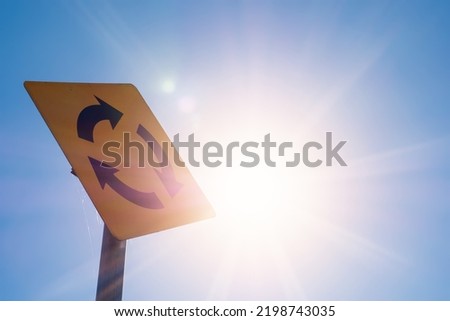 Yellow roundabout sign against clear blue sky and sun flare. Repetition of hot wave concept. Summer time.