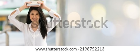 Young Asian woman holding books on top of the head in the university.