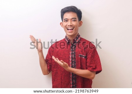 Portrait of an Asian man smiling and pointing his hand towards the side of the presentation and wearing a batik shirt. Isolated image on a white background