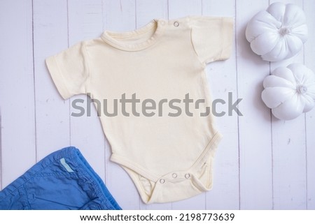 Yellow baby bodysuit mockup for logo, text or design on wooden background with pumpkins top view.