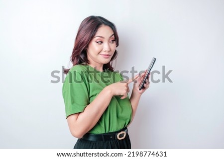 A portrait of a happy Asian woman is smiling and holding her smartphone wearing a green t-shirt isolated by a white background
