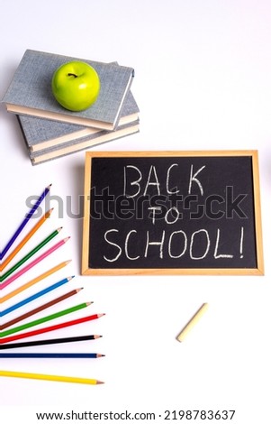 School still life: a blackboard with the inscription "back to school", a green apple, books and colored pencils on a white background