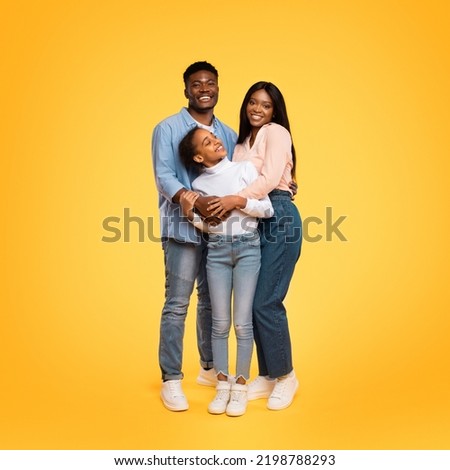 Happy family. Young african american parents with pretty daughter embracing while posing over yellow studio background. Parenthood and bonding concept