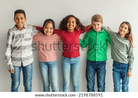 Cheerful Multiethnic Children Hugging Posing Smiling To Camera Indoors. Preteen Boys And Girls Standing Together Over Gray Wall. Childhood And Friendship Concept. Royalty-Free Stock Photo #2198788591
