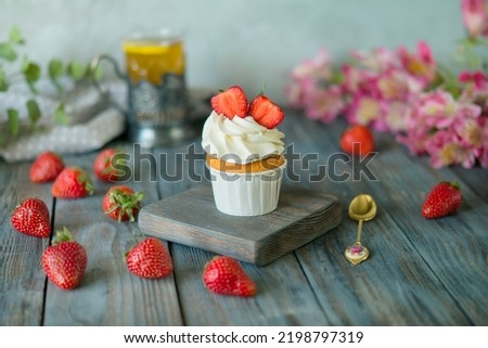 Vanilla muffin with strawberries, a cup of hot tea, on a wooden table, side view, copy space. Seasonal, morning Sunday breakfast and rest.


