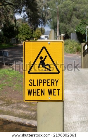 Slippery when wet yellow warning sign on the metal bridge in the park