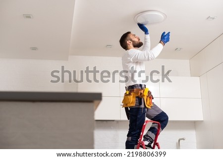 Electrician worker installation electric lamps light inside apartment. Construction decoration concept. Royalty-Free Stock Photo #2198806399
