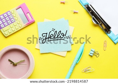 Sticky note with word HELLO, calculator, clock and stationery on yellow background