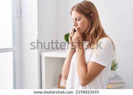 Young blonde girl talking on smartphone with worried expression at home Royalty-Free Stock Photo #2198823695