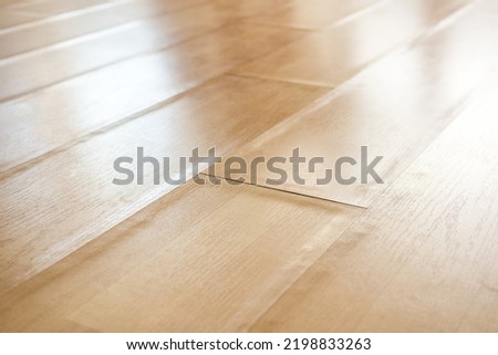 Swollen laminate flooring from flood or water damage, perspective view. Close up of light beige buckling laminate boards with bent edge pieces. Floor damage texture. Selective focus in center. Royalty-Free Stock Photo #2198833263