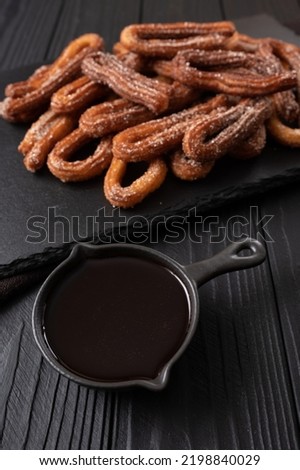 Homemade churros with chocolate on a dark wooden rustic background.