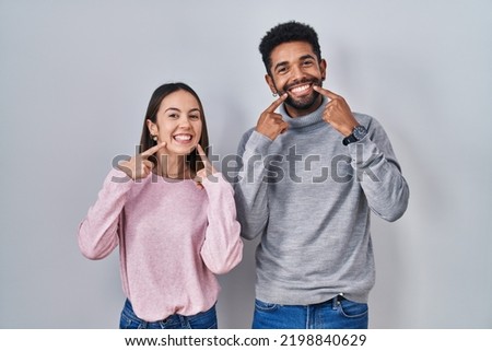 Young hispanic couple standing together smiling with open mouth, fingers pointing and forcing cheerful smile 