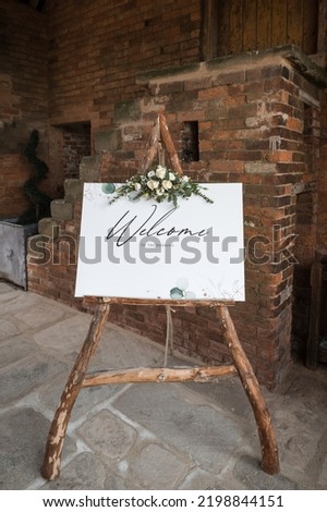 Welcome sign to wedding, wooden frame natural wood with flowers bouquet floral display.  Standing outside wedding venue to welcome guests.