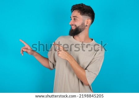 bearded caucasian man wearing casual T-shirt over blue background smile excited directing fingers look empty space