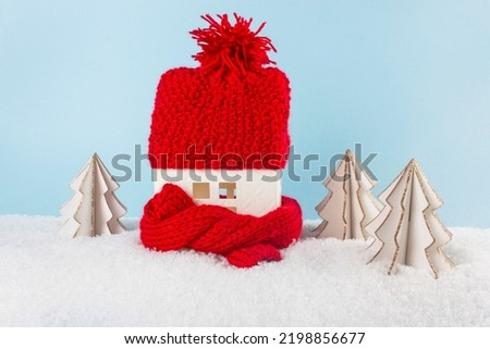 Figure of house and warm clothes on the snow against blurred lights. Concept of heating season. European energy crisis concept. Copy space.