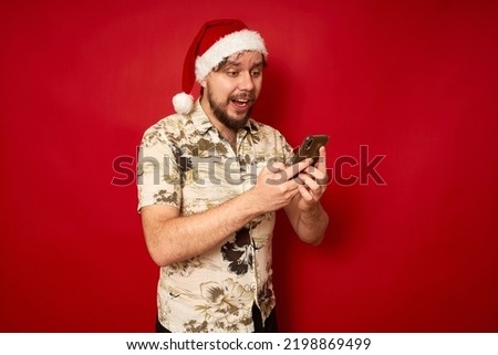 Excited young traveler tourist man in summer clothes, santa hat using mobile cell phone typing sms message isolated on red background. Passenger traveling abroad on holidays Air flight journey concept