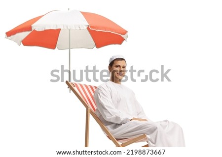 Man in ethnic clothes sitting in a beach chair under umbrella isolated on white background     