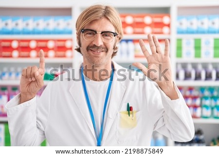 Caucasian man with mustache working at pharmacy drugstore showing and pointing up with fingers number six while smiling confident and happy. 