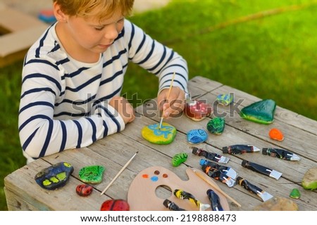 A detailed picture of a child's hands drawing a fungus on a stone with acrylic paints. Home hobbies are authentic. Artwork on stones.