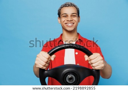 Young cheerful happy fun man of African American ethnicity 20s he wearing red shirt hold steering wheel pretend driving isolated on plain pastel light blue cyan background. People lifestyle concept Royalty-Free Stock Photo #2198892855
