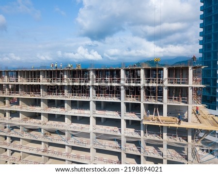 Drone view of the construction site, builders on the top floor of a building under construction against the backdrop of mountains on a sunny day