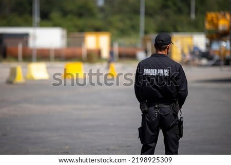 Border police officer is seen from the back guarding the a border. Royalty-Free Stock Photo #2198925309