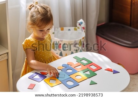 A little girl playing with wooden shape sorter toy on the table in playroom. Educational boards for Color and Shapes sorting for toddler. Learning through play. Developing Montessori activities. Royalty-Free Stock Photo #2198938573