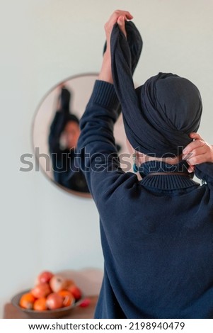 Religious Jewish woman puts a shawl on her head in front of a mirror. Back view Royalty-Free Stock Photo #2198940479