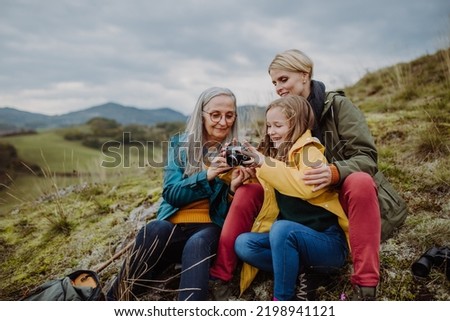 Senior woman taking picture of her daughter and granddaughter on top of hill in autumn day.