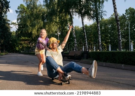 Cheerful girl and mother playing with skateboard in the park.