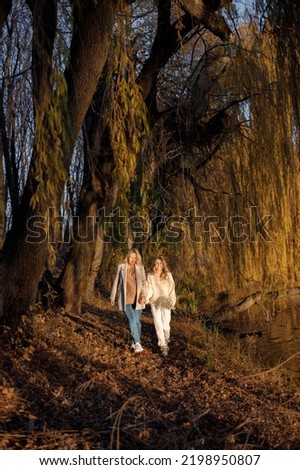 Adult daughter and her pregnant mom holding hands while standing in autumn park
